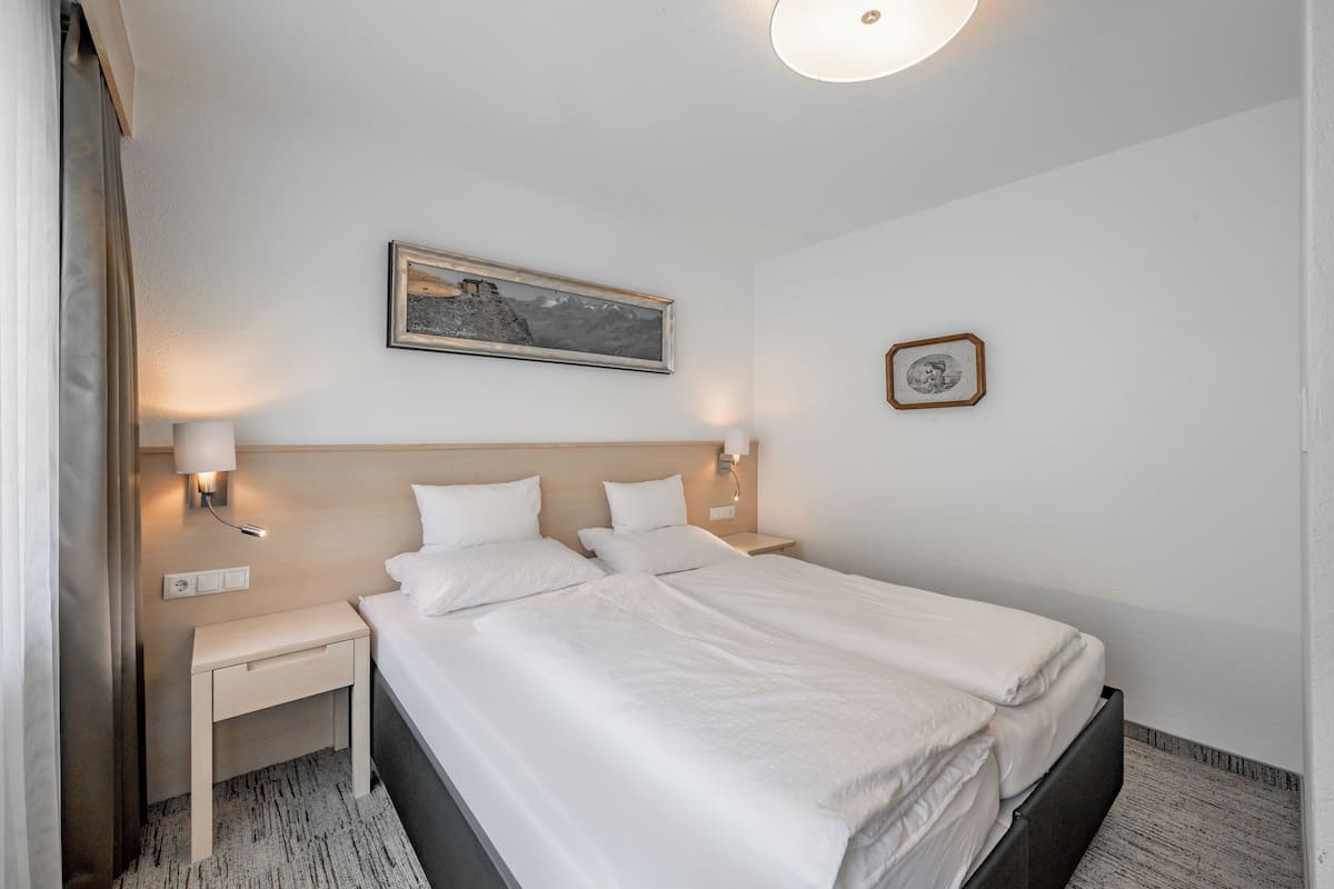A hotel room with a large bed, bedside tables, a nightstand, a wall-mounted lamp, and a framed picture.