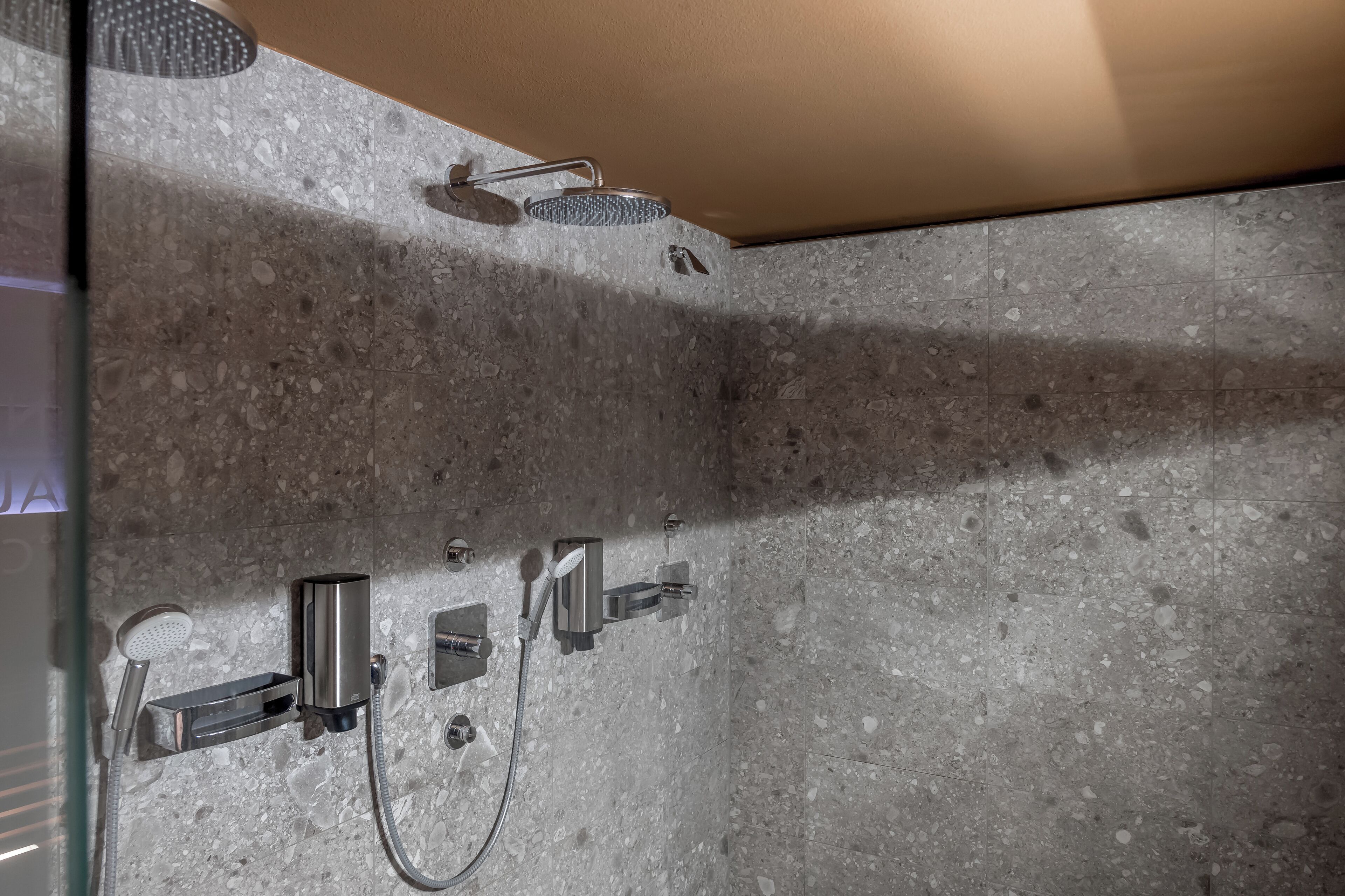 A shower area with a handheld showerhead, a wall-mounted showerhead, and a handheld showerhead with a rain shower attachment.