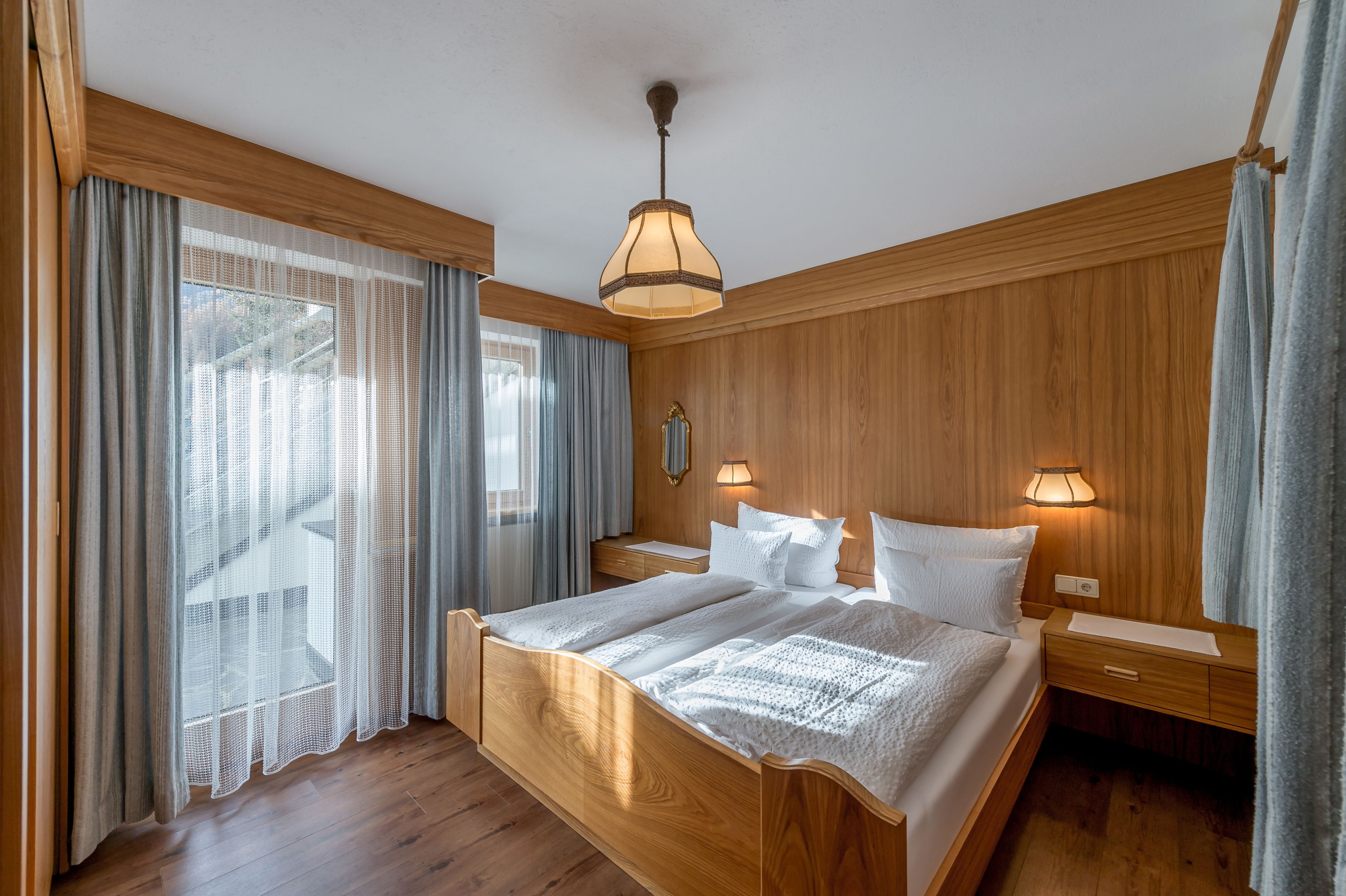 A wooden-paneled bedroom with a large bed, two bedside tables, and a hanging light fixture.