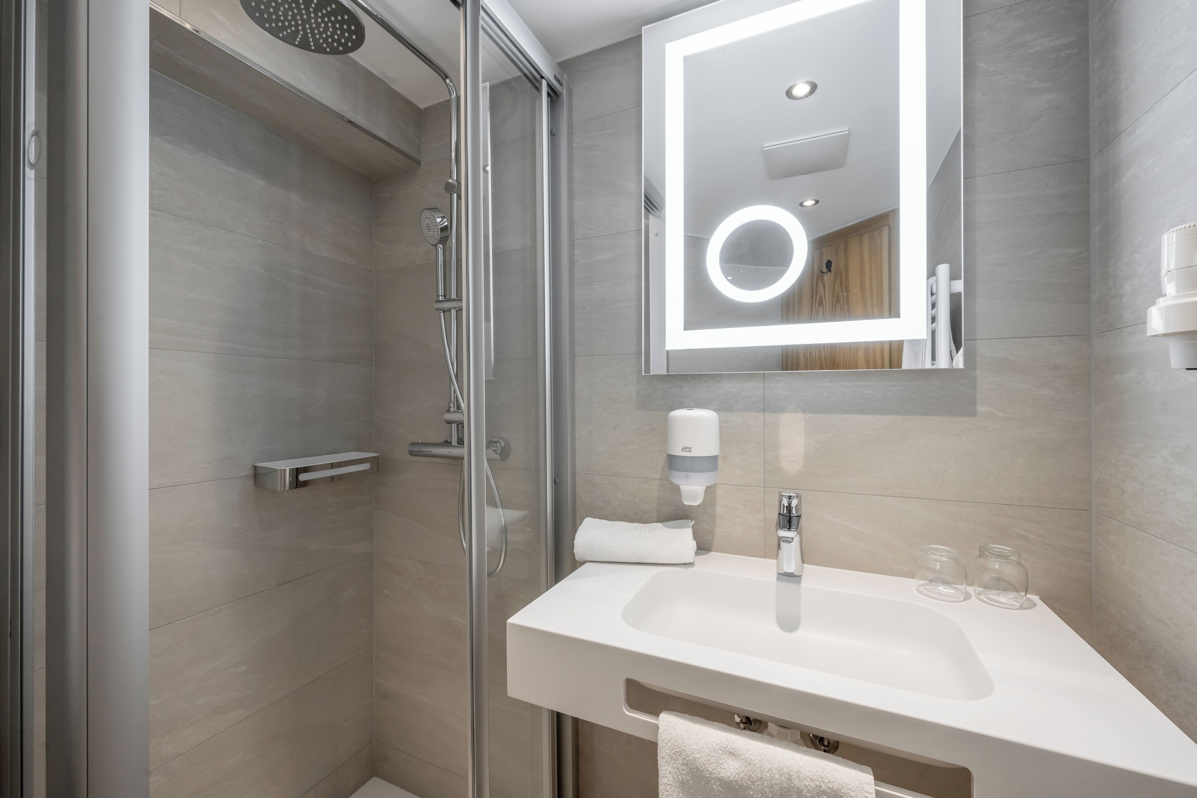 Ein modernes Badezimmer mit Duschkabine aus Glas, einem weißen Waschbecken mit Spiegel und einem Handtuchhalter.