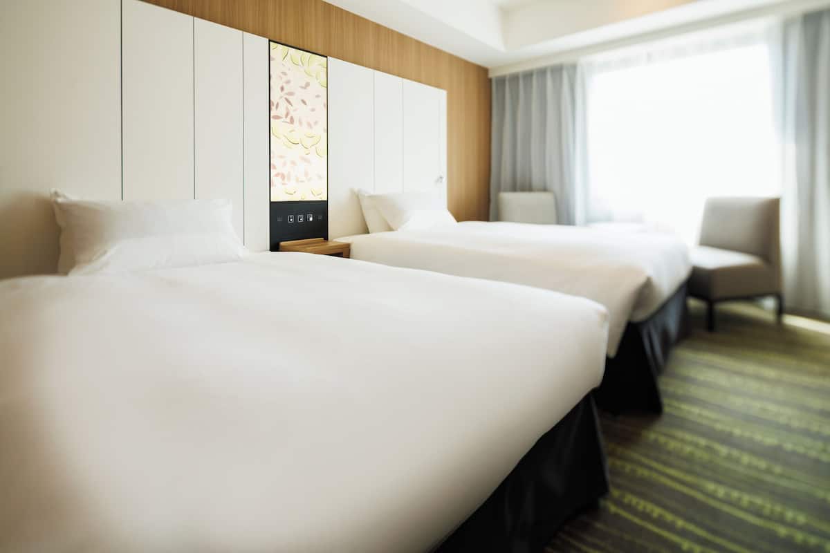 A hotel room with two beds, a wooden headboard, a large window with curtains, and a carpeted floor.