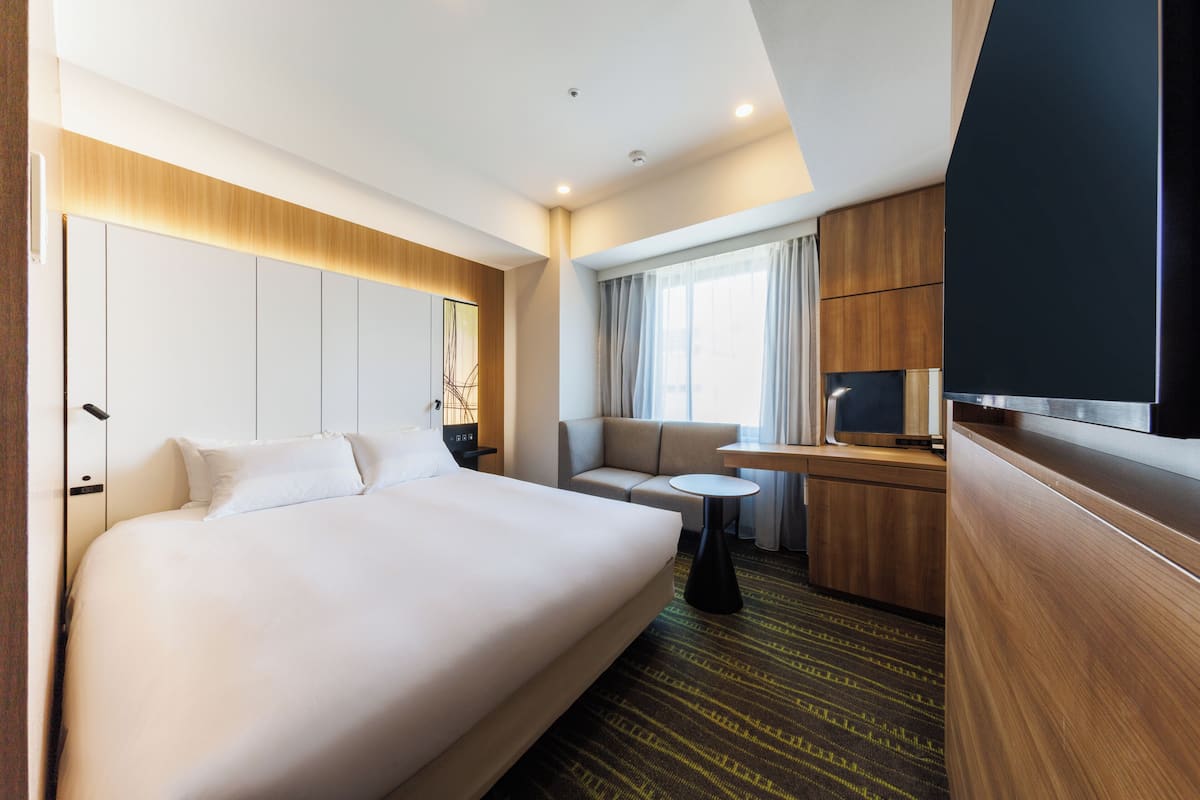A hotel room with a large bed, a sofa, a small table, a TV, and wooden paneling.