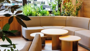 Un canapé moderne aux lignes courbes, accompagné de deux tables rondes, dans un espace lumineux et agrémenté de plantes.