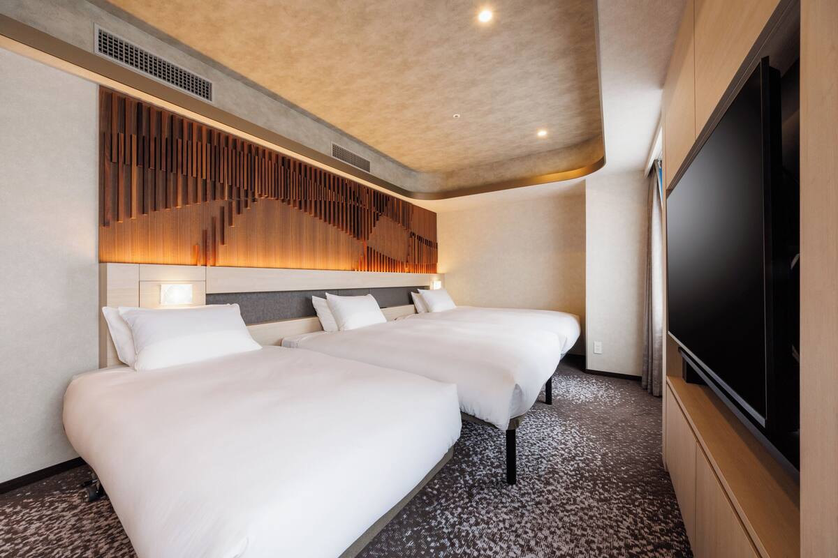 A hotel room with two beds, a large flat-screen TV, and a modern wall design.