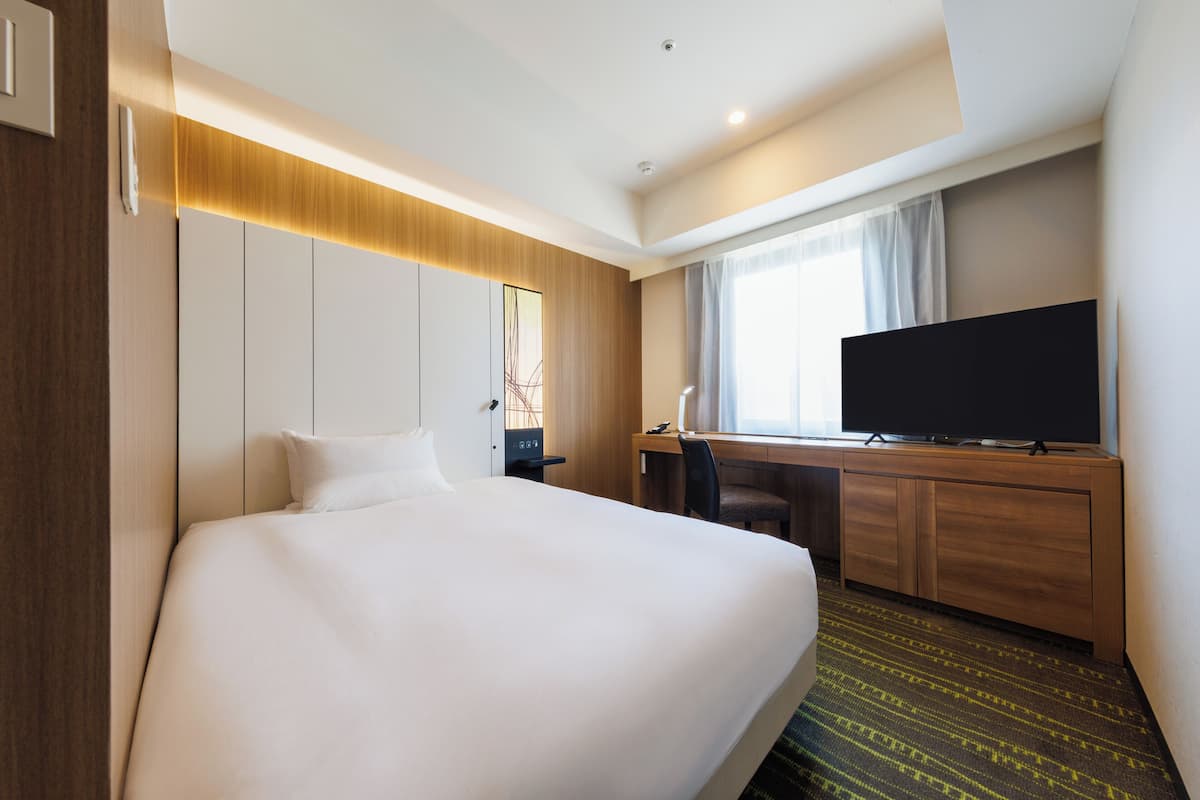 A hotel room with a large bed, a desk with a flat-screen TV, and a window with curtains.