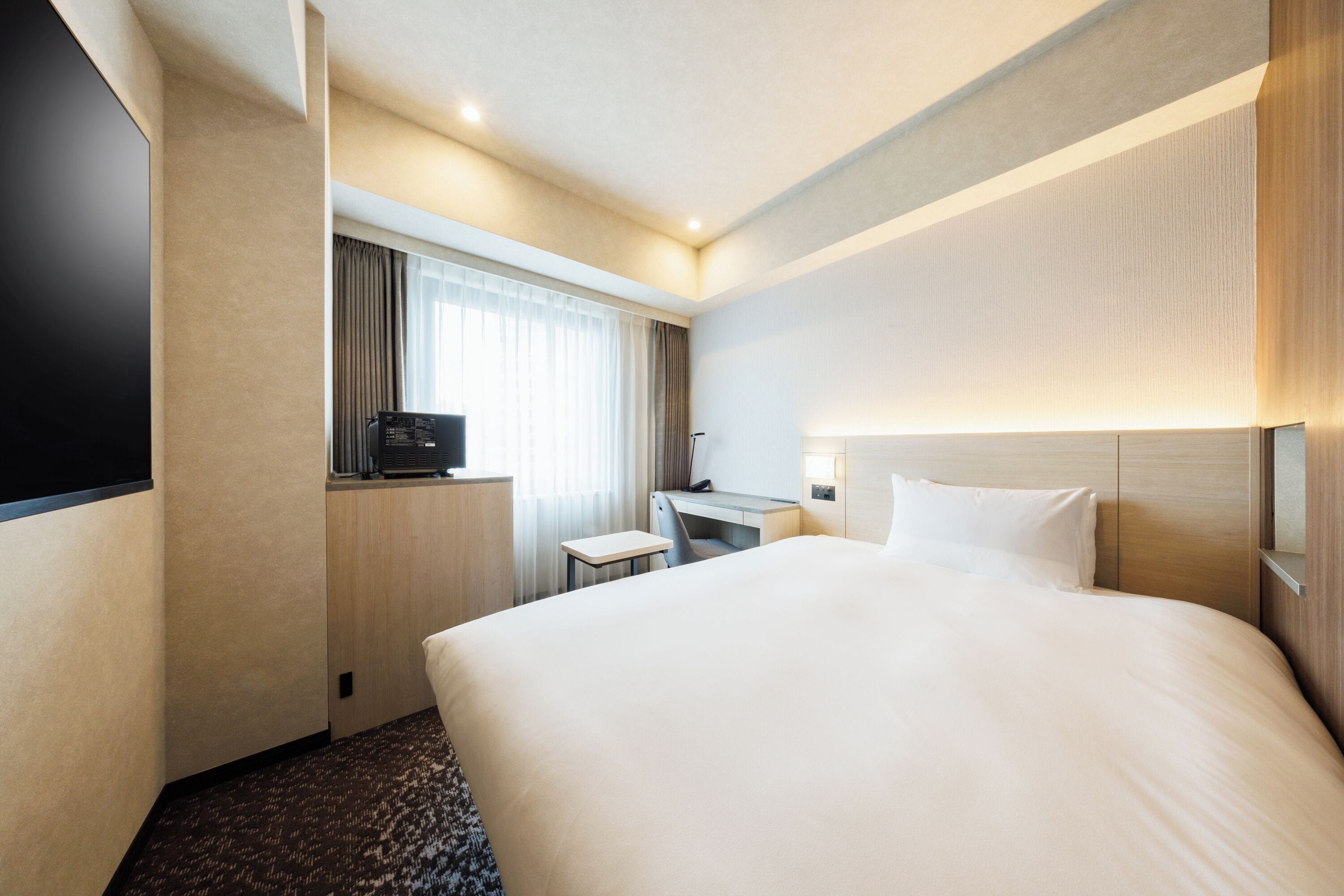 A hotel room with a large bed, a desk, a television, and a window with curtains.