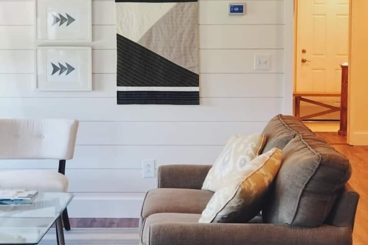 A living room with a sofa, a chair, and a coffee table. There are wall-mounted arrows and a framed picture on the wall.