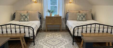 A cozy attic bedroom with two beds, a wooden table, a nightstand, and a patterned rug.