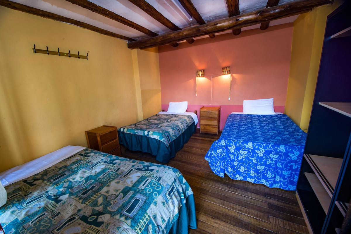Una habitación con dos camas individuales, suelo de madera y techo inclinado con vigas a la vista.