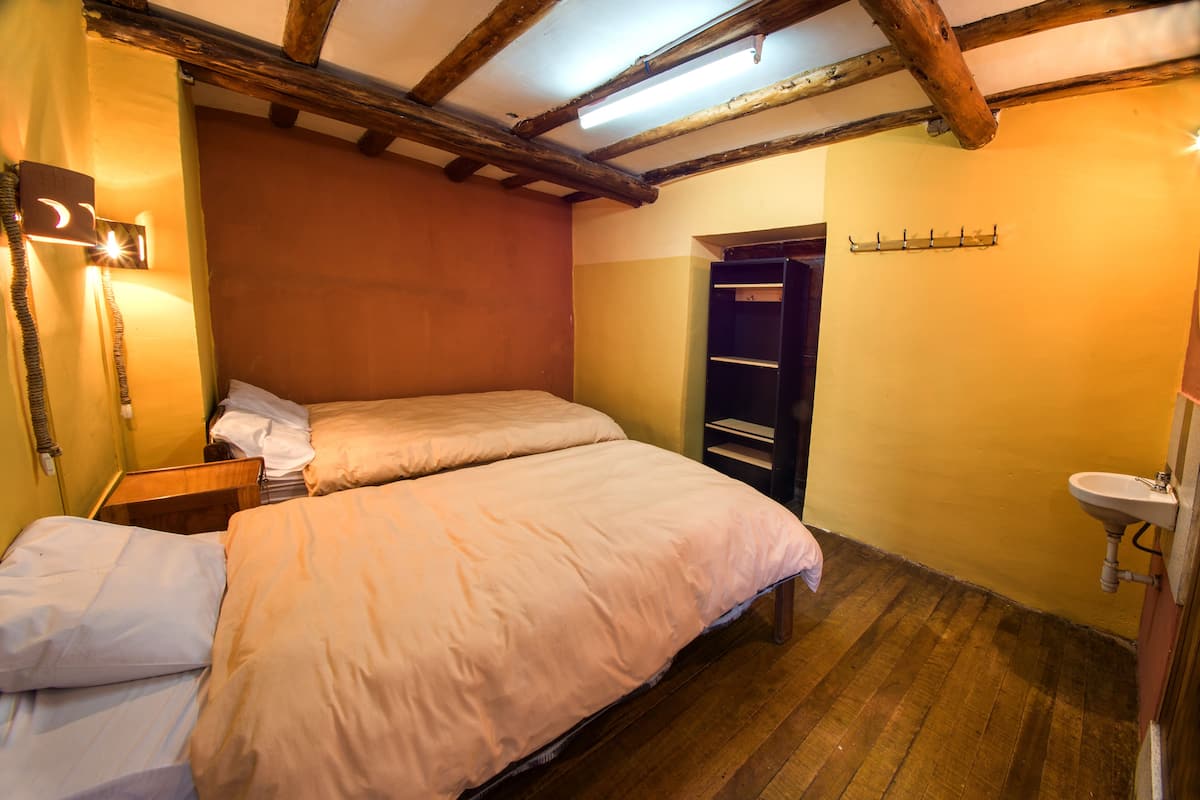 Una habitación con dos camas, techo de madera, una mesita de noche pequeña, un armario y un lavabo.