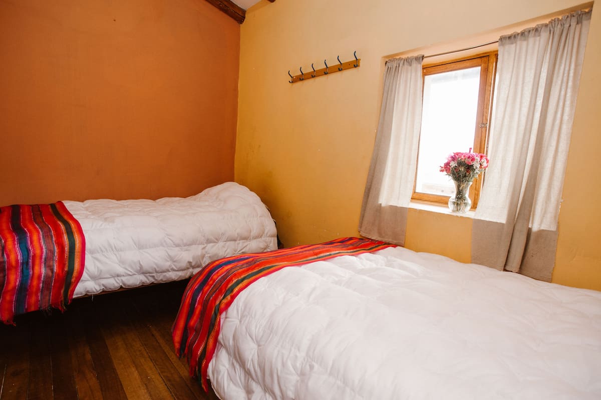 Una habitación con dos camas, una ventana con cortinas y un perchero de madera.