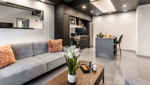 Una sala de estar moderna con un sofá gris, una mesa de centro de madera, y una cocina con armarios oscuros y una isla central.