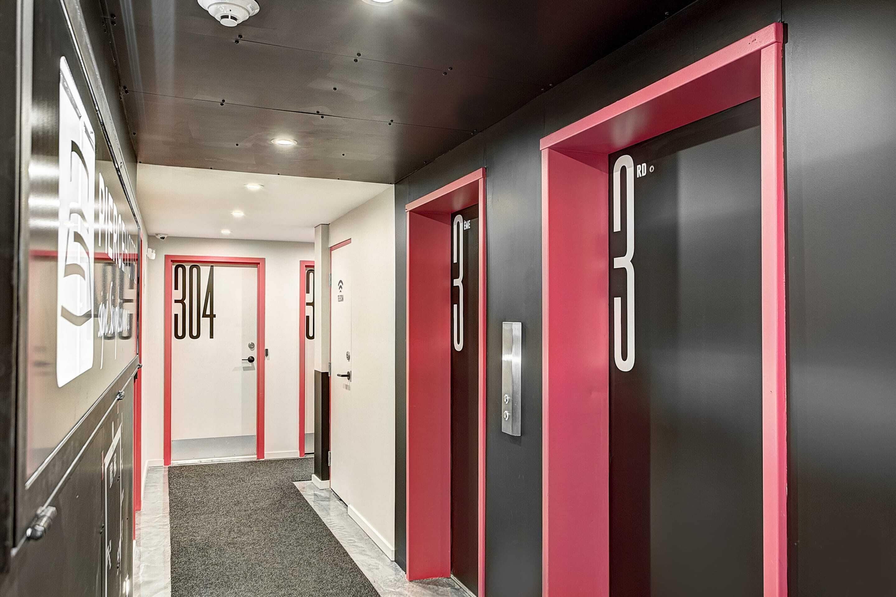 A hallway with doors numbered 304 and 303, featuring a modern design with red accents and a grey carpet.