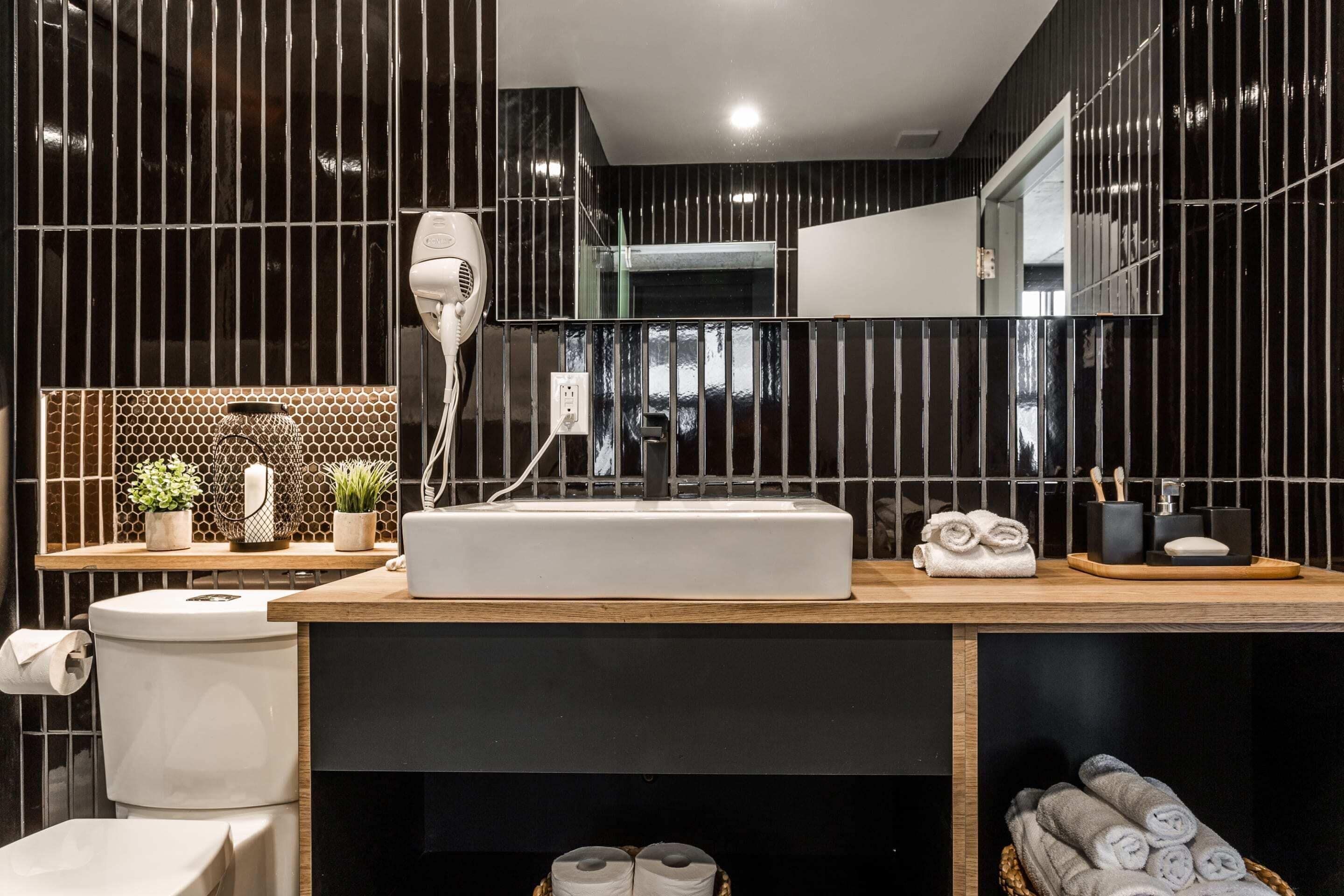 A modern bathroom with a large mirror, a white sink, and a hairdryer on the counter.
