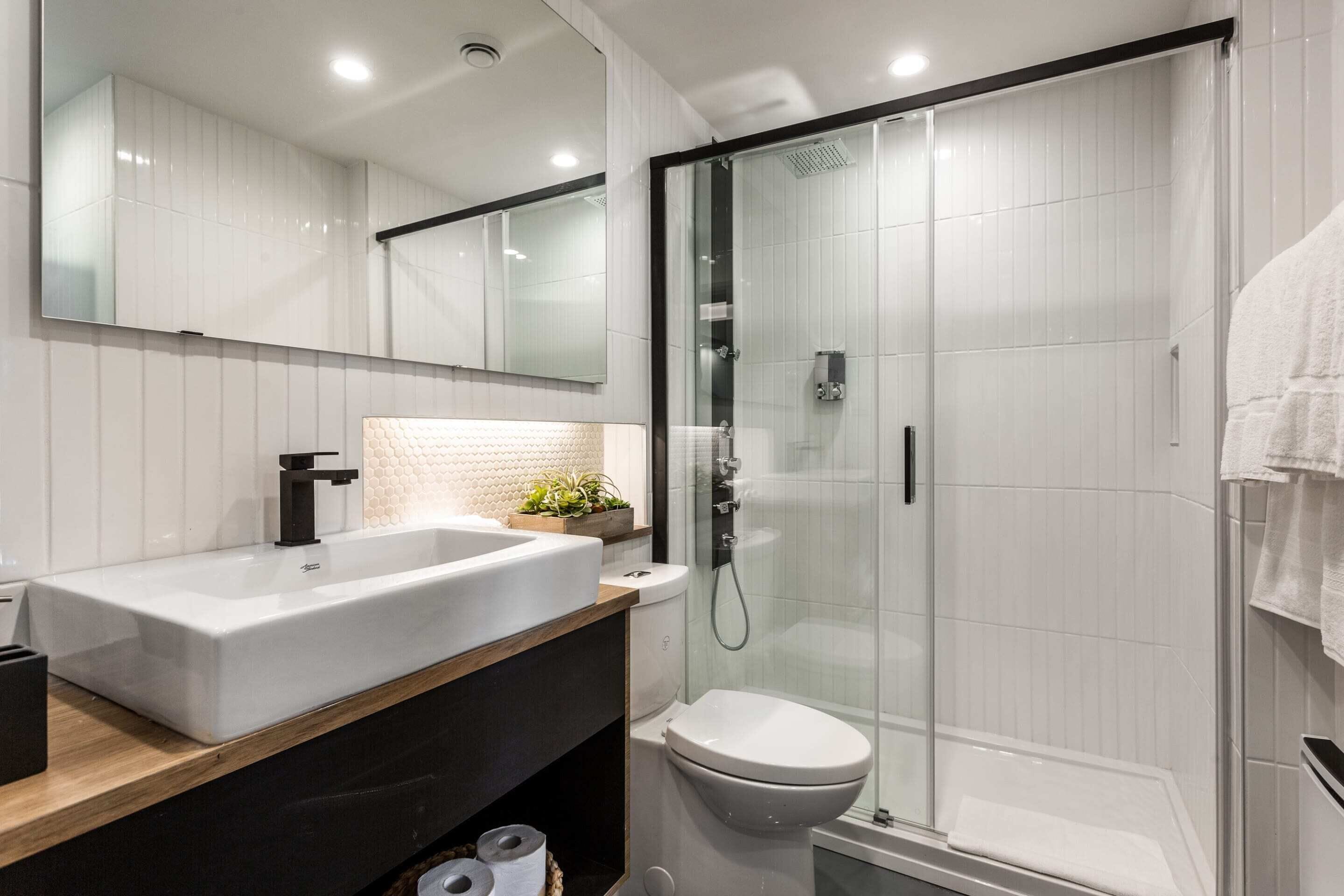 A modern bathroom with a large white sink, a toilet, and a glass-enclosed shower.