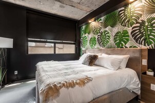 Un dormitorio moderno con una cama grande, techo de concreto y pared decorada con hojas tropicales.