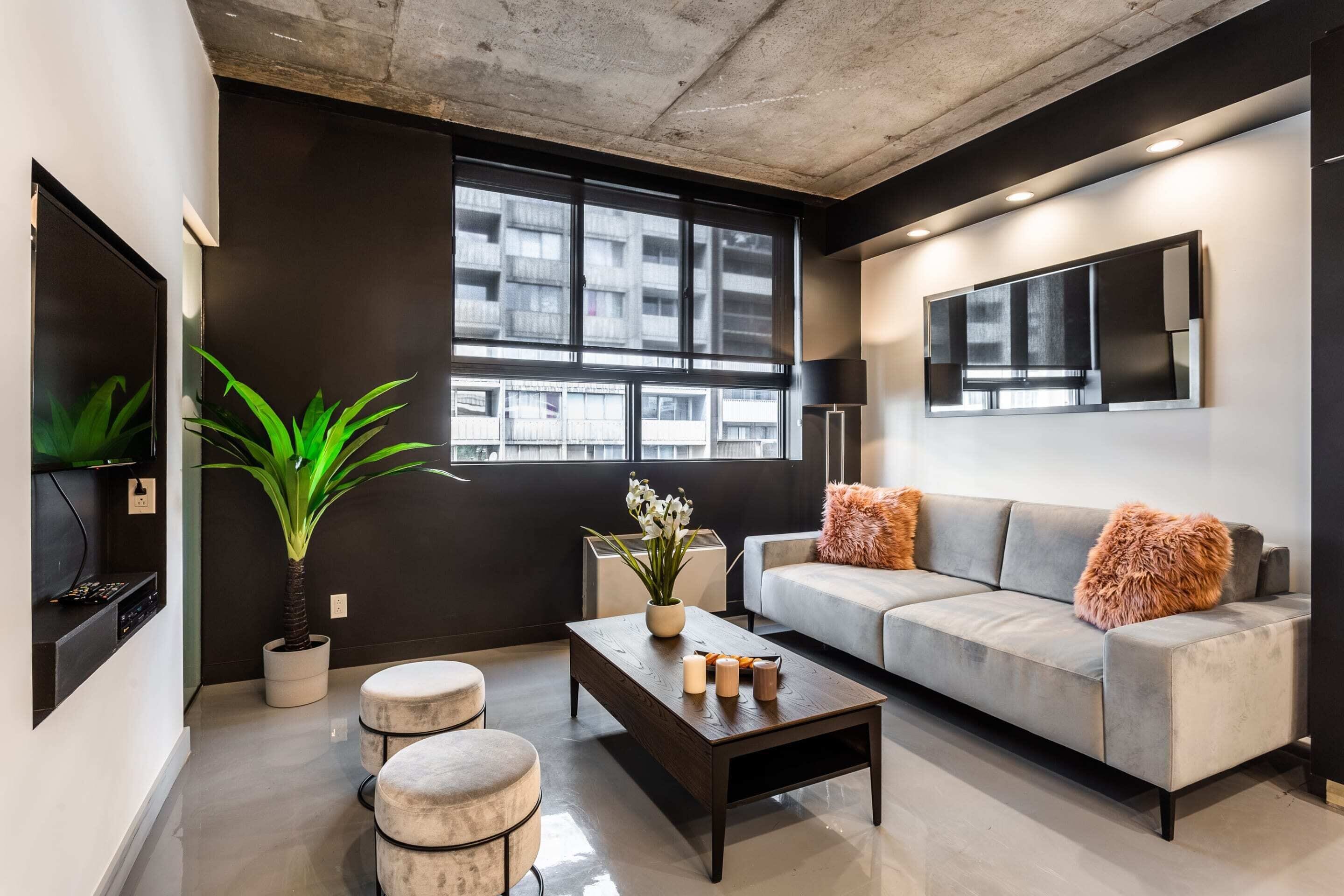 Una sala de estar moderna con un sofá gris, una mesa de centro, una planta en maceta y un ventanal con vistas a la ciudad.