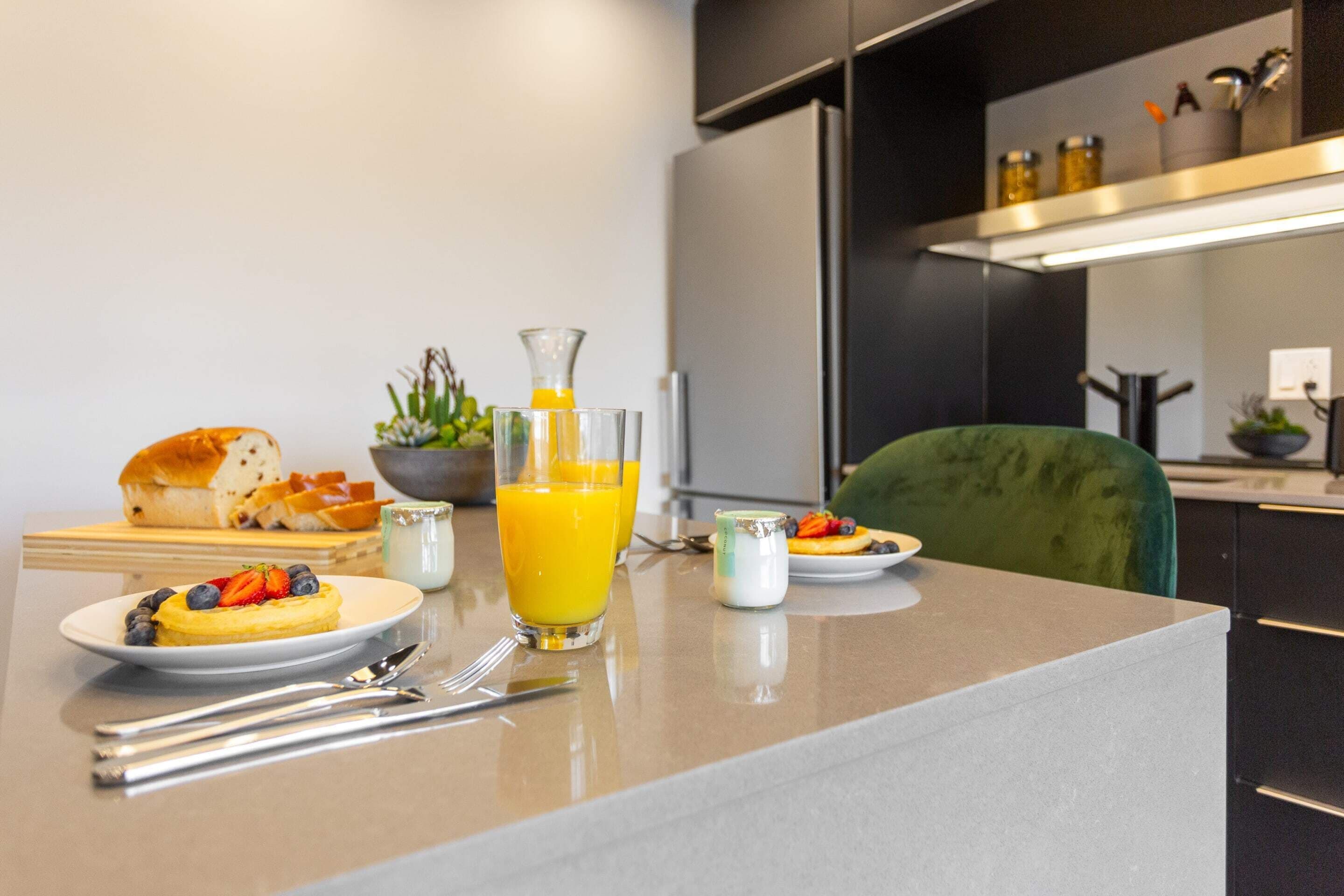 A breakfast setting with a plate of pancakes topped with strawberries and blueberries, a glass of orange juice, and a bowl of cereal.