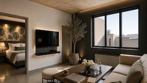 Una sala moderna con una televisión de pantalla plana, una mesa de centro, un sofá y un ventanal con vistas a la ciudad.
