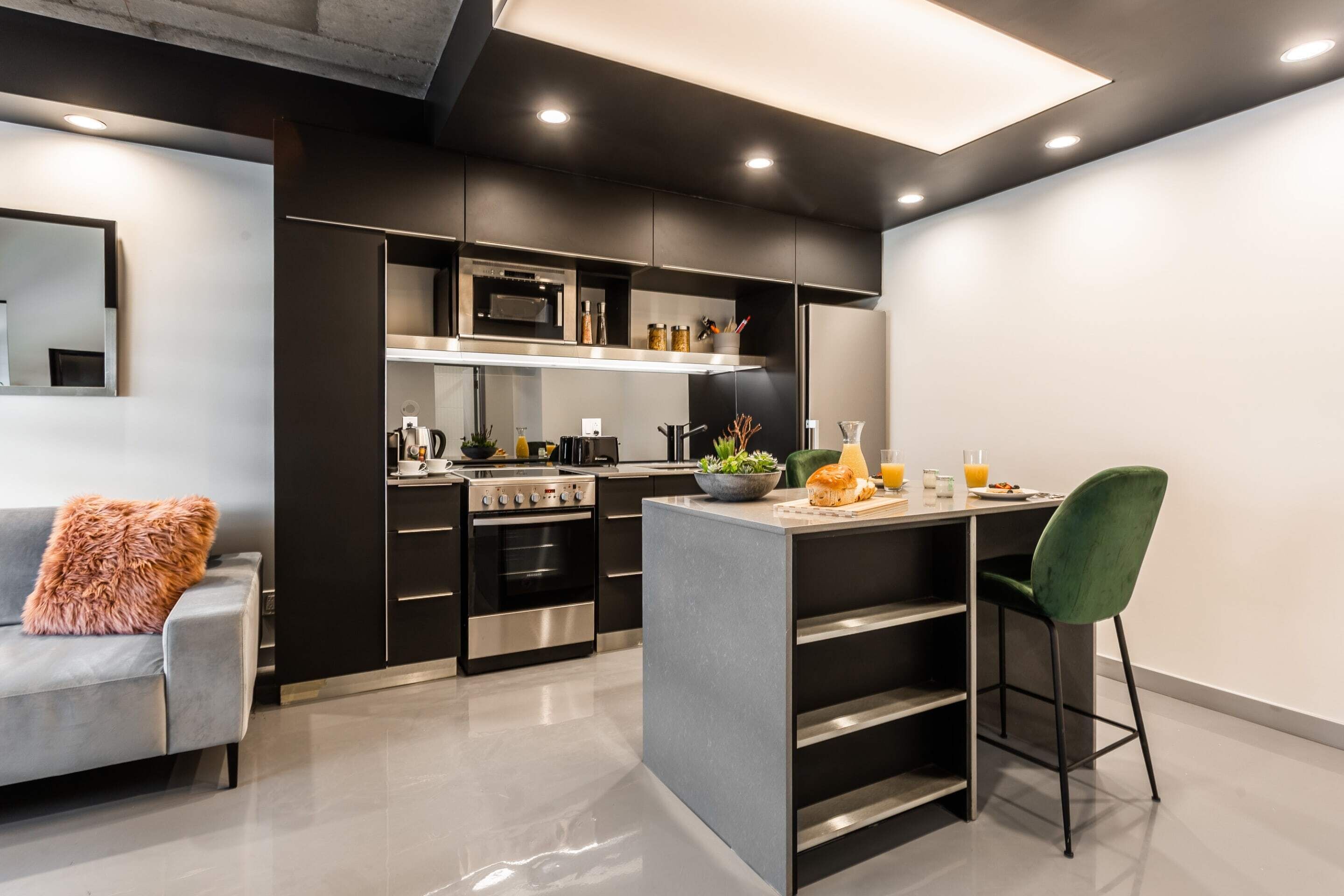 Een moderne keuken met zwarte kasten, roestvrijstalen apparatuur en een centraal eiland met barstoelen.
