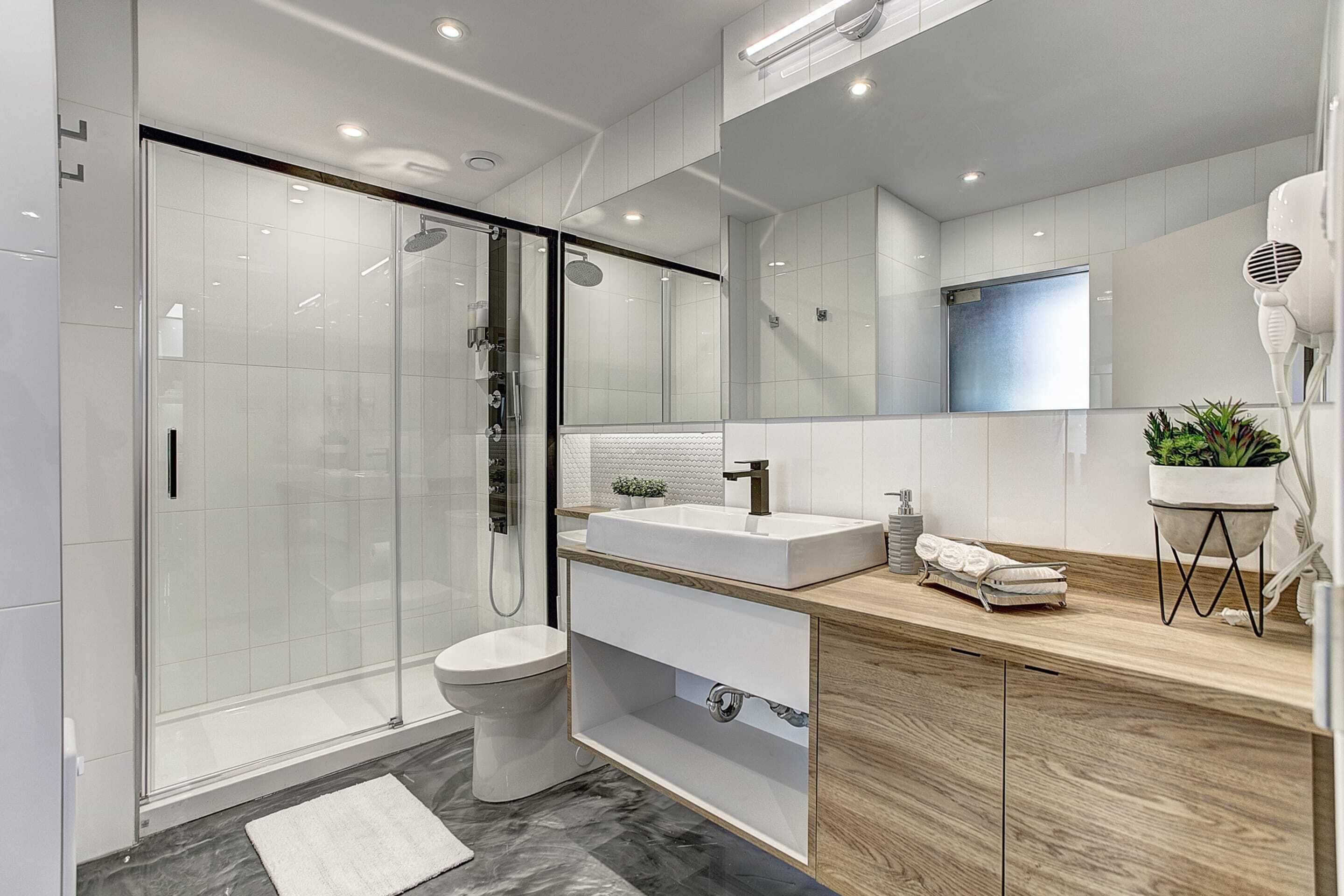 A modern bathroom with a glass shower enclosure, a white sink, and a wooden vanity.
