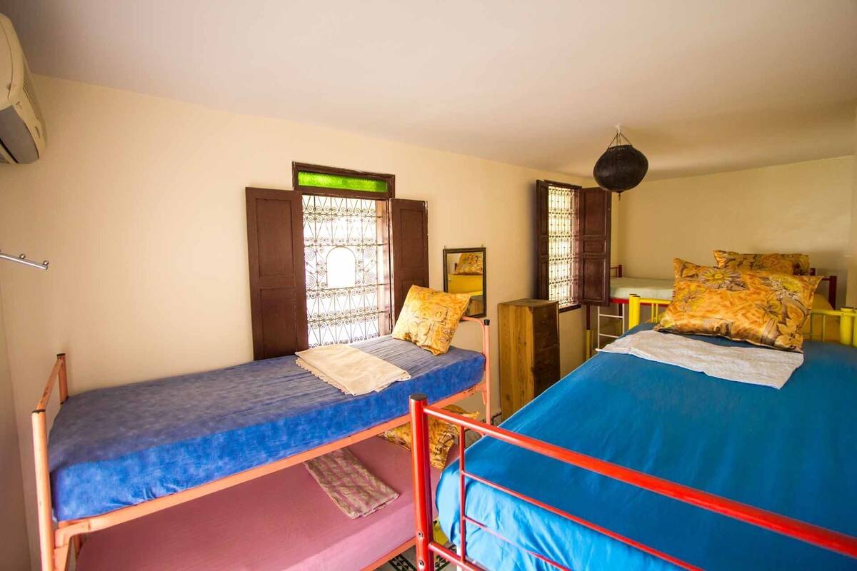 A dormitory room with two bunk beds, a small table, a mirror, and a hanging light fixture.