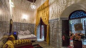 Quarto tradicional marroquino com cama, paredes estampadas e porta decorativa.
