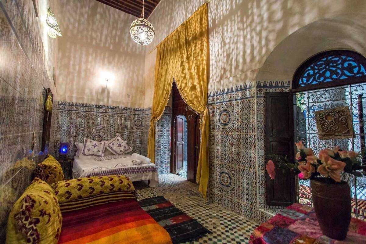 A traditional Moroccan room with a bed, patterned walls, and a decorative door.