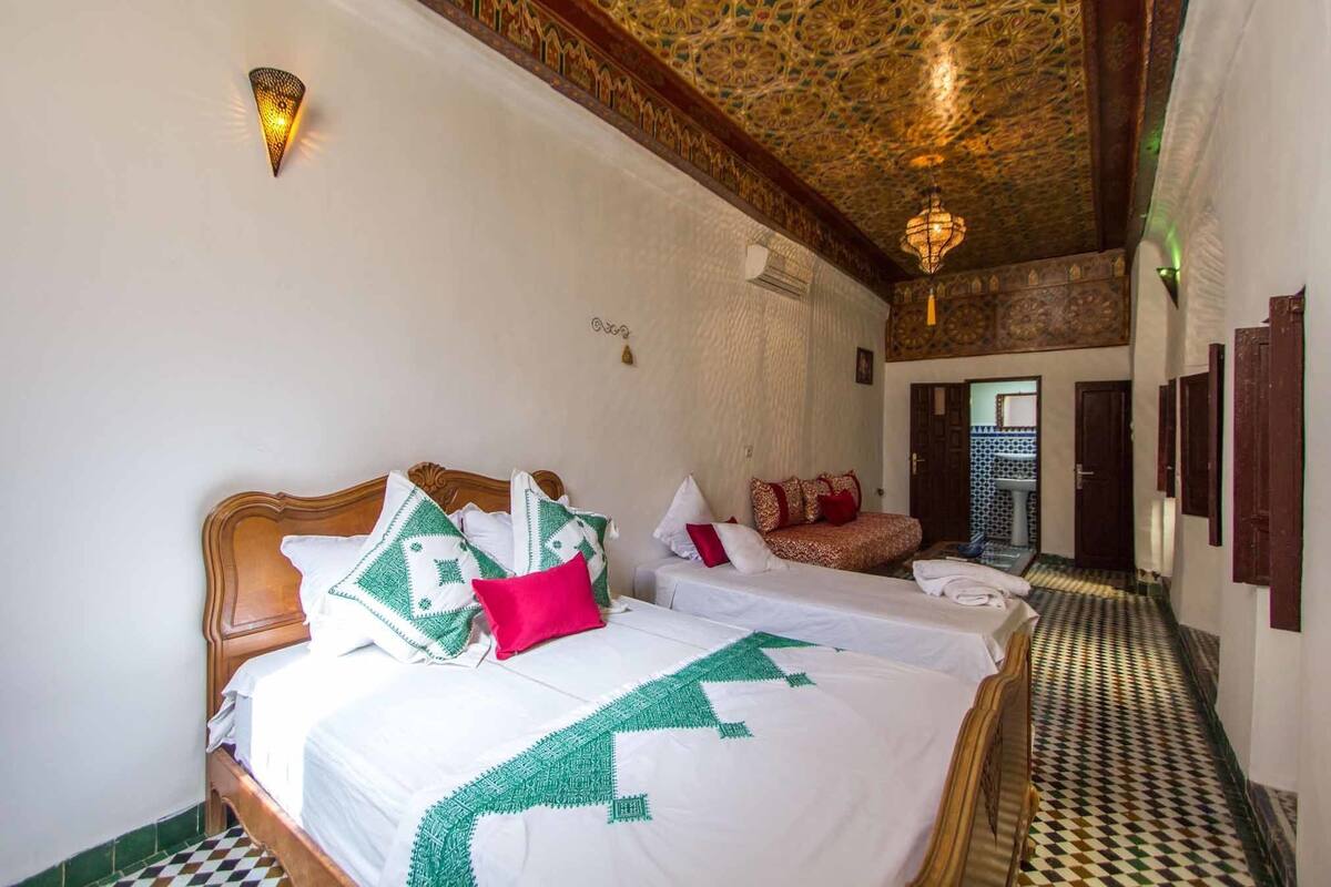 A hotel room with two beds, a patterned ceiling, and a hallway leading to a bathroom.
