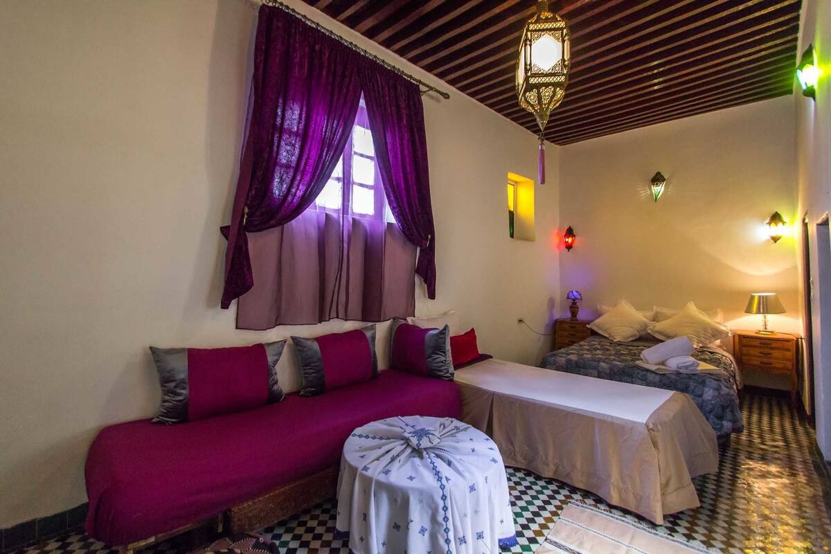 A small, cozy room with a sofa, two beds, a small table, and a patterned floor.