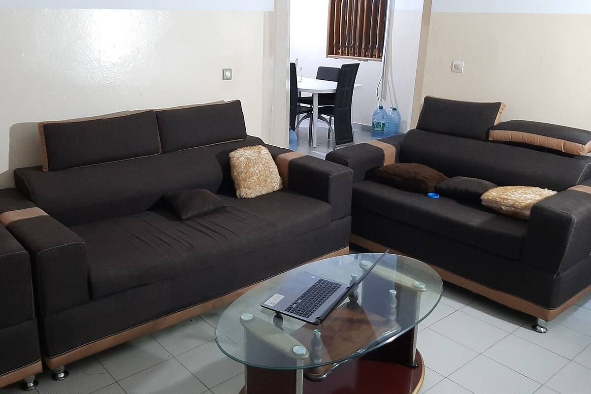 A living room with two dark sofas, a glass coffee table, and a dining area in the background.