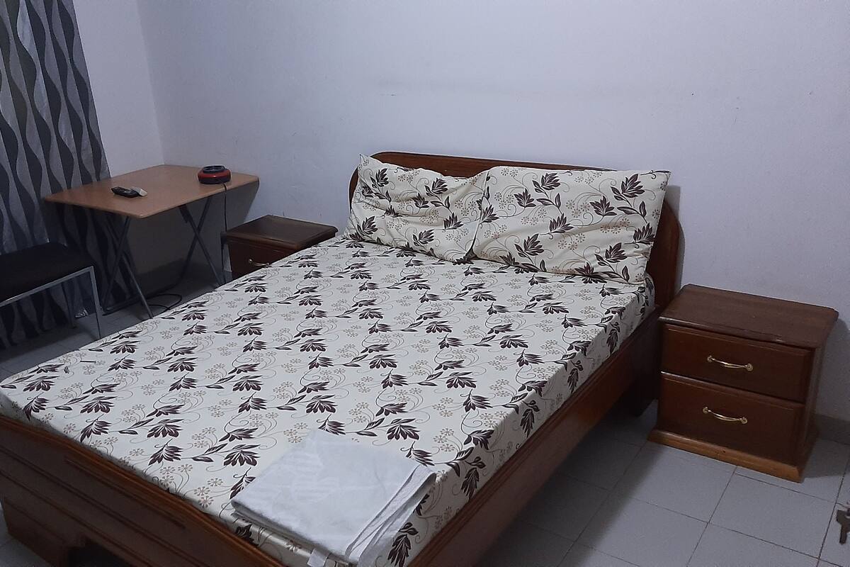 A bedroom with a bed, a desk, a chair, and a nightstand.