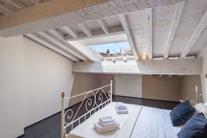 A bedroom with a skylight, a bed with white linens, and a view of a dome in the distance. - Santa Croce Apartments by Mmega (Florence)