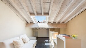Een moderne loft slaapkamer met een hoge plafond, een witte bank, een klein bureau, en uitzicht op een koepelstructuur door een dakraam.