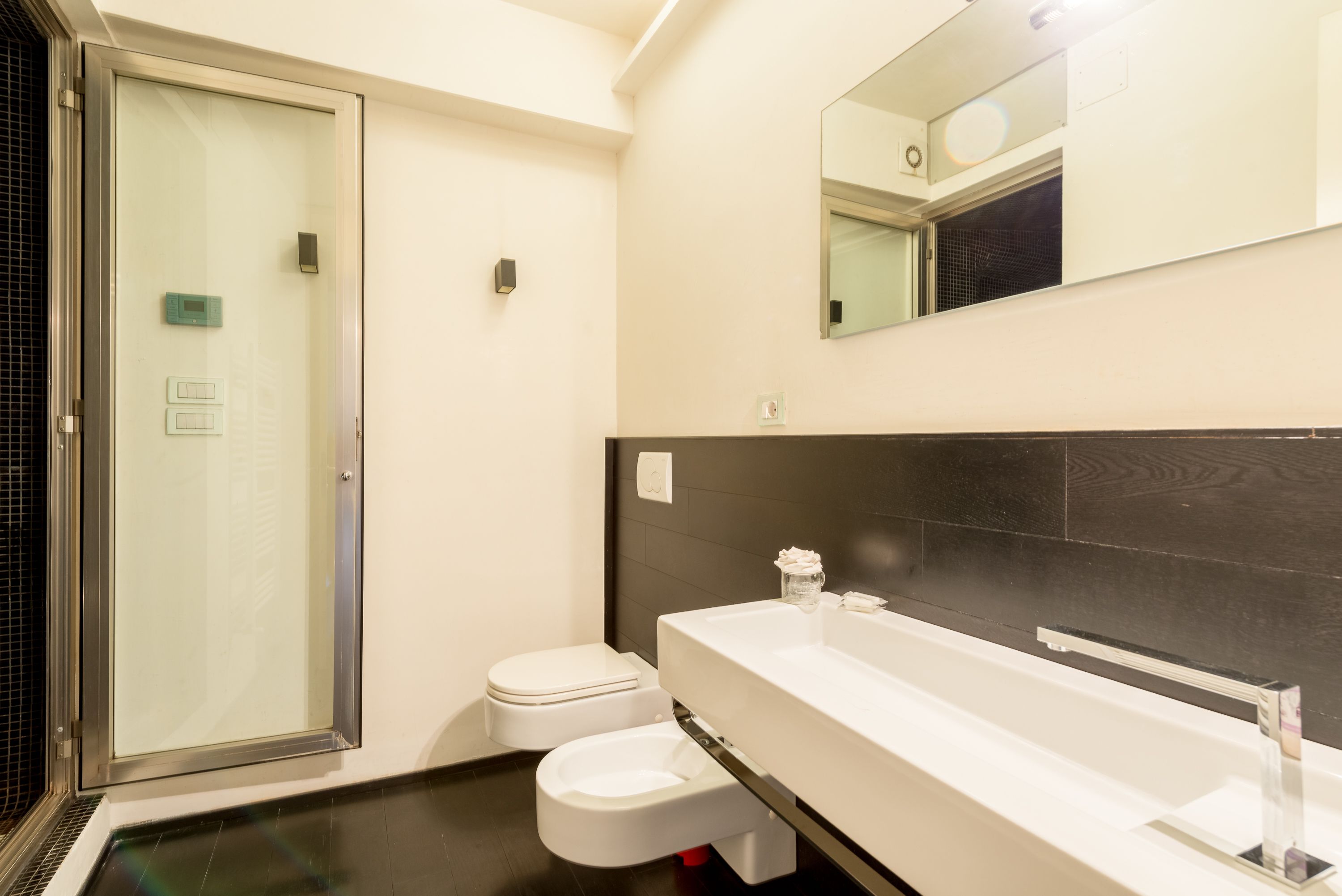 A modern bathroom with a glass shower enclosure, a white toilet, and a large sink with a mirror above.