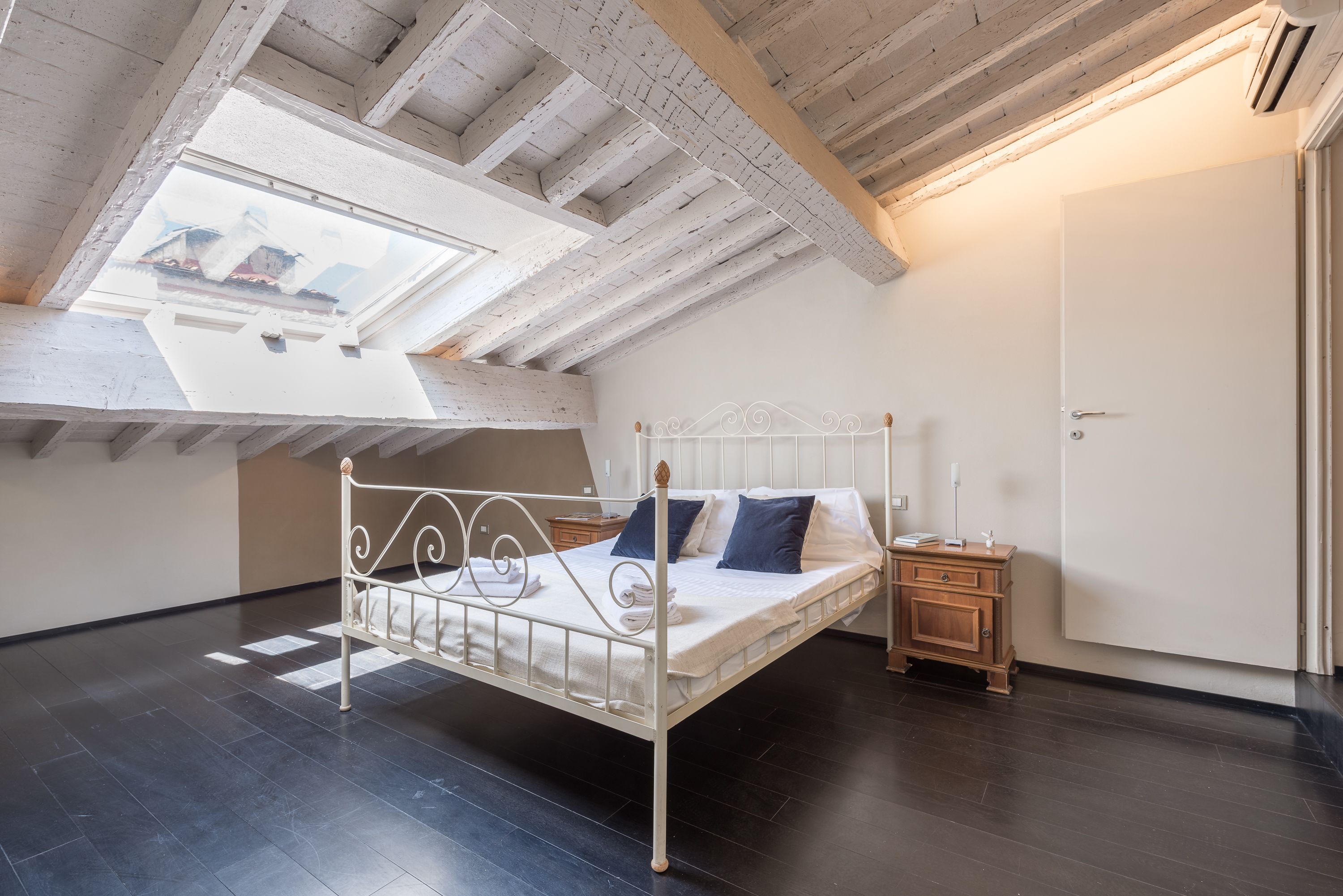 A bedroom with a skylight, a metal bed frame, a bedside table, and a wardrobe.