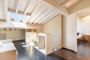 Un dormitorio tipo loft moderno con vigas de madera a la vista, tragaluces, una cama blanca, un escritorio y vistas a un edificio con cúpula.