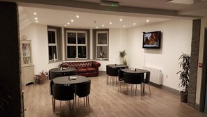 A spacious room with a red leather sofa, two round tables with chairs, and a television mounted on the wall. - The Dalby Rooms (Margate)