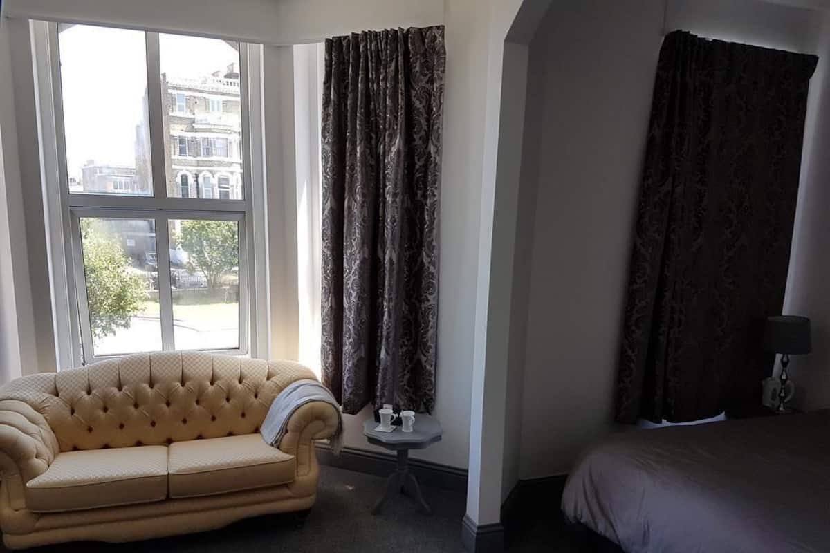 Quarto de hotel com uma janela grande, um sofá, uma mesa pequena com duas chávenas e uma cama.