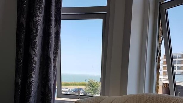 A room with a large window, a tufted sofa, and a view of the sea. - The Dalby Rooms (Margate)