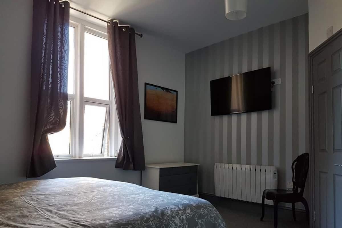 Quarto com cama, cadeira, televisão e radiador.