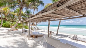 Una playa con una pérgola de madera, sillas de descanso y una zona arenosa.