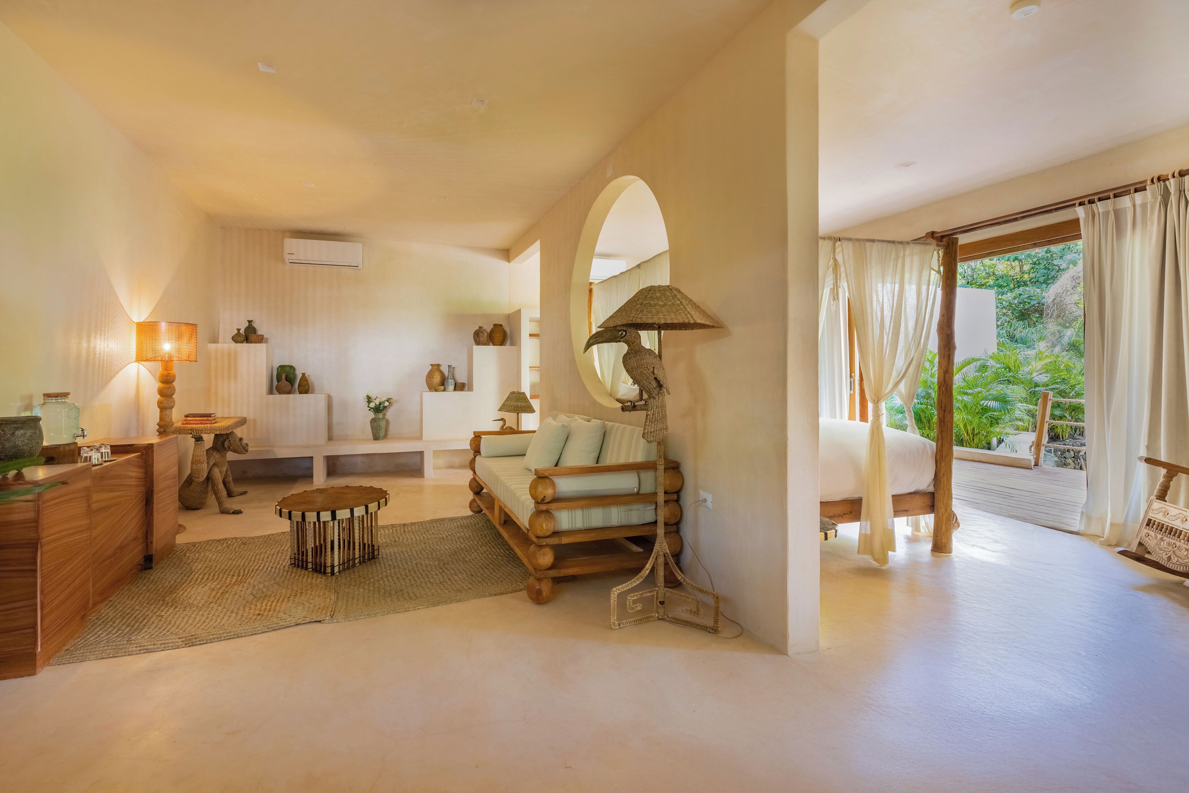 A spacious room with a wooden sofa, a small round table, a lamp, and a bed with curtains.