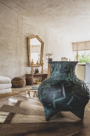A room with a rustic wooden floor, a large mirror, a decorative vase, and a plant.