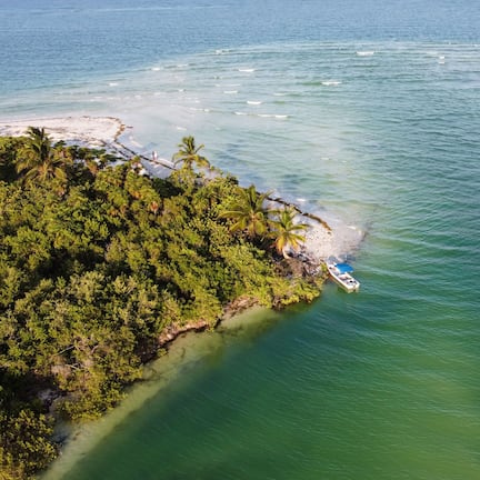 An aerial view of a tropical island with a boat docked near the shore, surrounded by clear waters and dense vegetation.