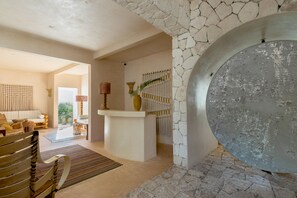 A spacious living area with a stone fireplace, a round mirror, and a seating area with a sofa and a wooden bench.