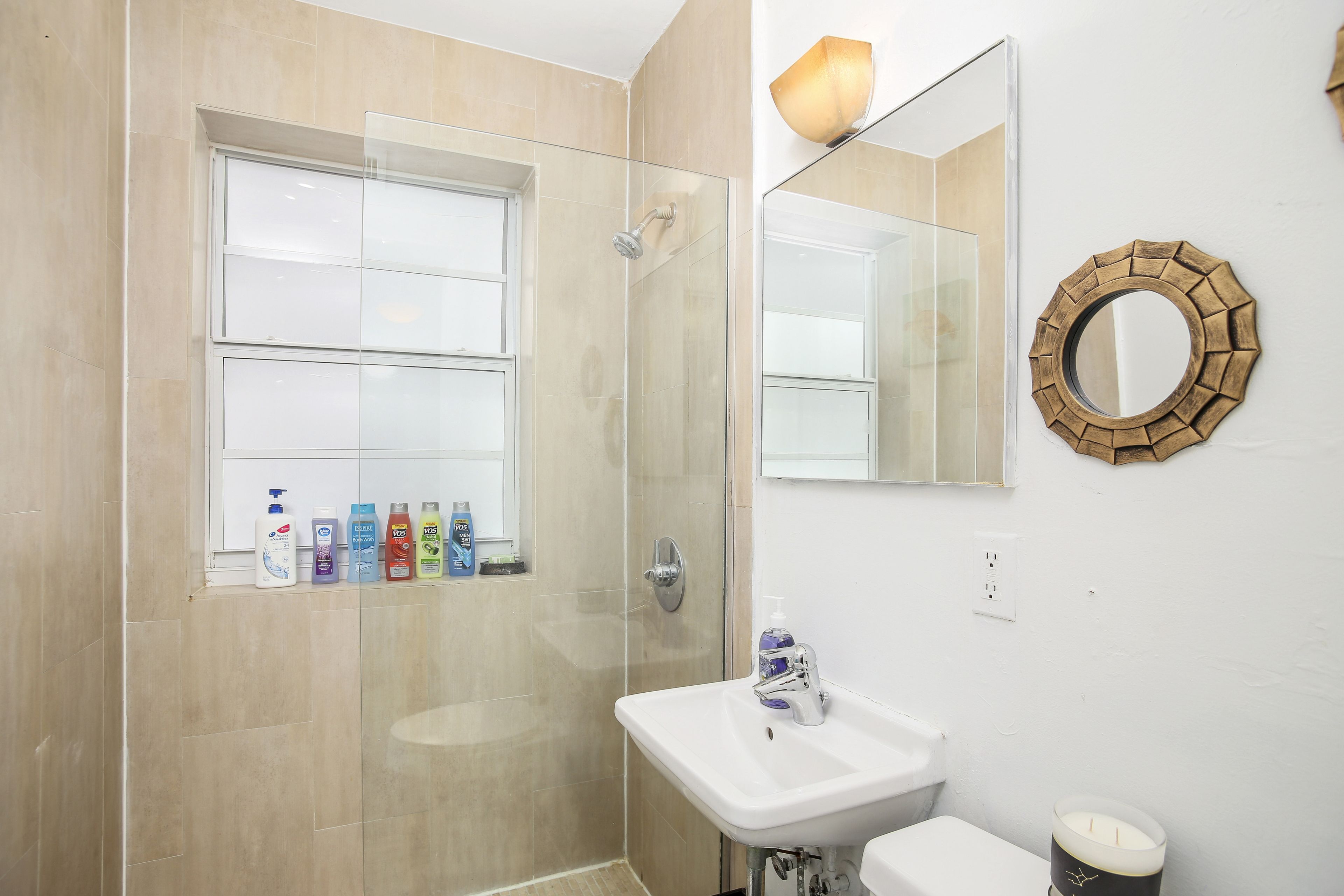 Un baño con mampara de vidrio, lavamanos y espejo.