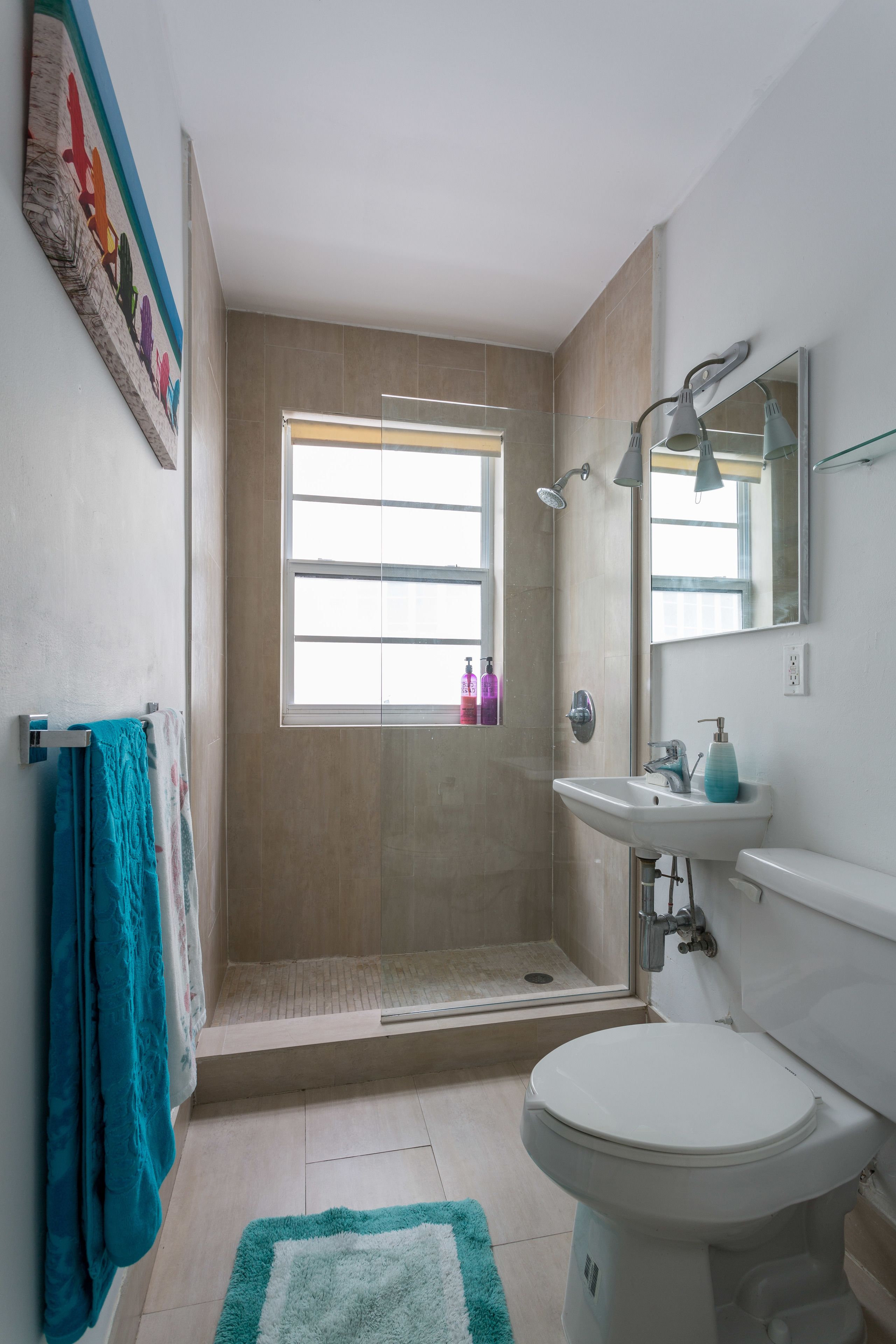 A bathroom with a shower, toilet, sink, and a window.