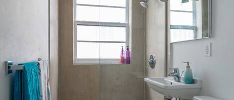 A bathroom with a shower, toilet, sink, and a window.