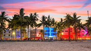 A beachside hotel with palm trees and colorful buildings during sunset. - Apartment on the Beach (Miami Beach)